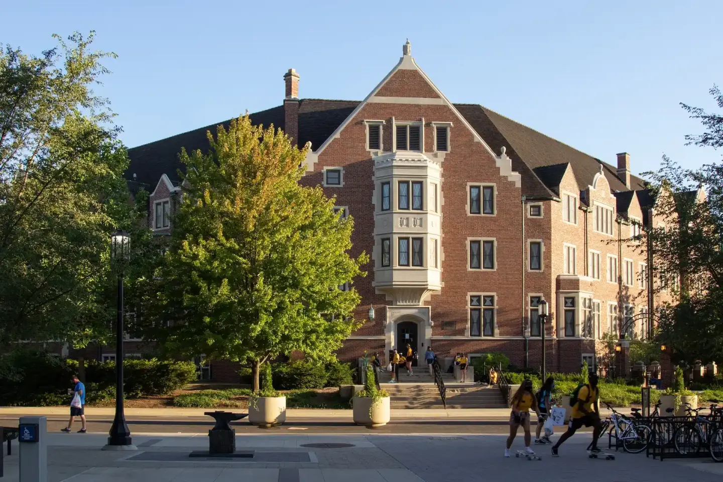 Brick building with a gabled roof and a stone entrance, with students walking outside on a sunny day