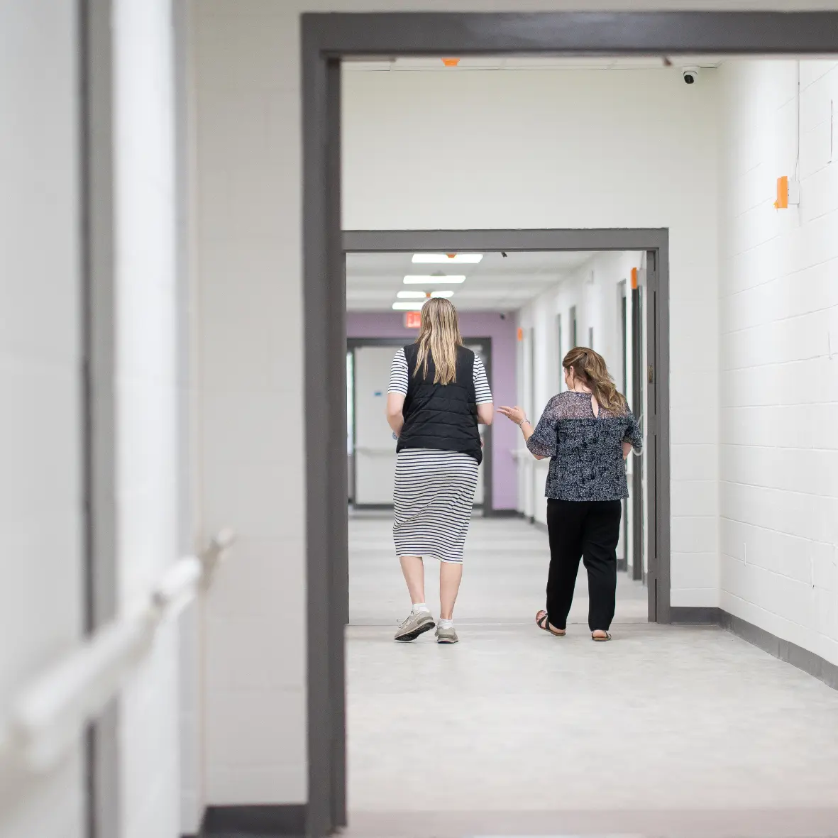 Long hallway with white block walls, gray door frames, and a purple accent wall at the far end
