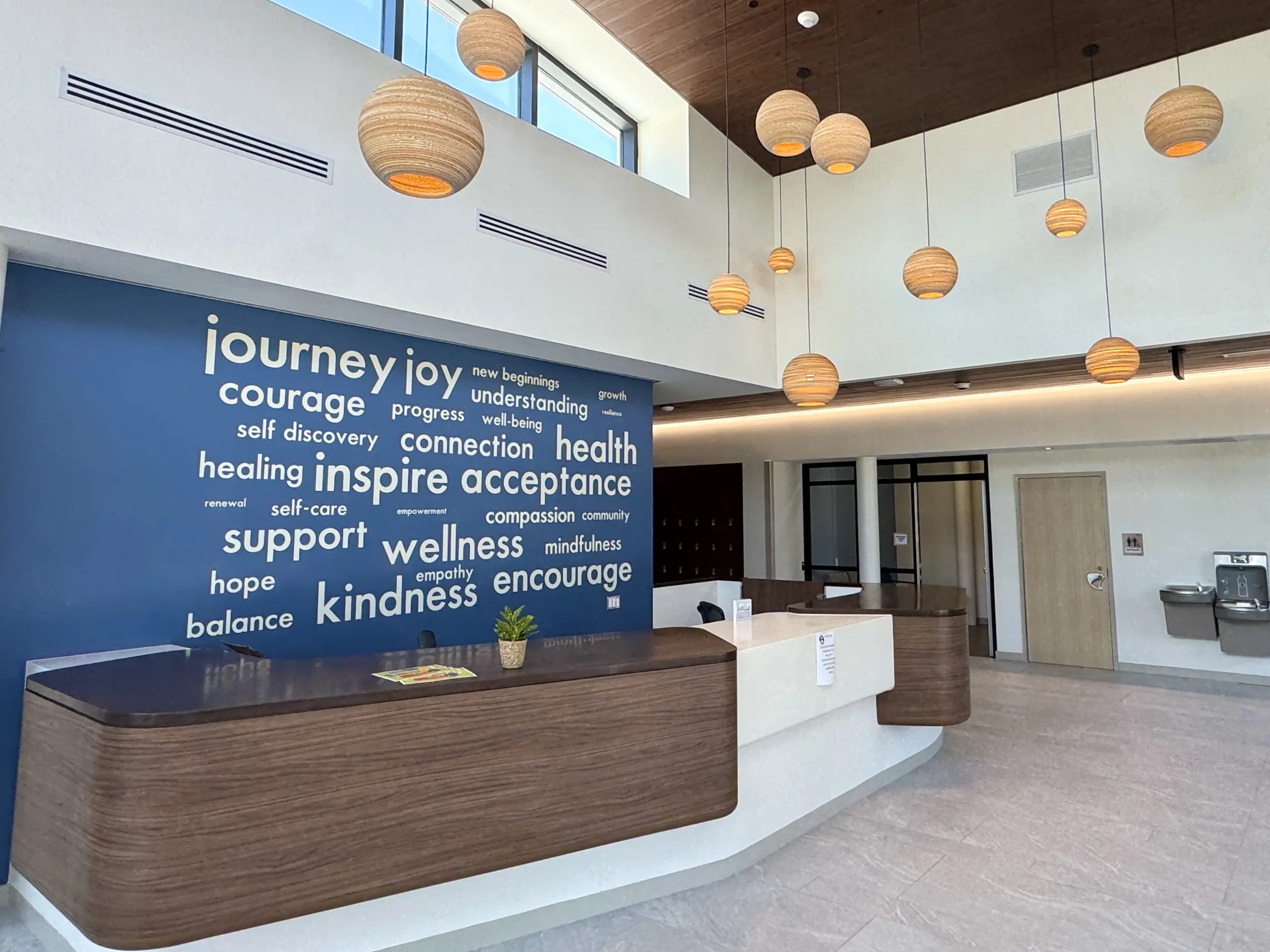 Bright two-story lobby with a reception desk and a blue wall of words such as journey, joy, and wellness