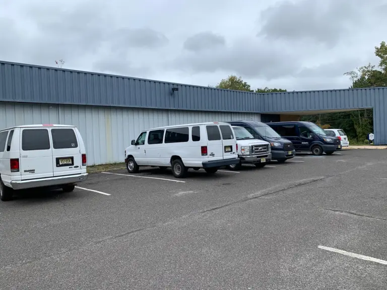 Gray metal-clad treatment center building with covered entrance and parked vans, one marked MGBHPC