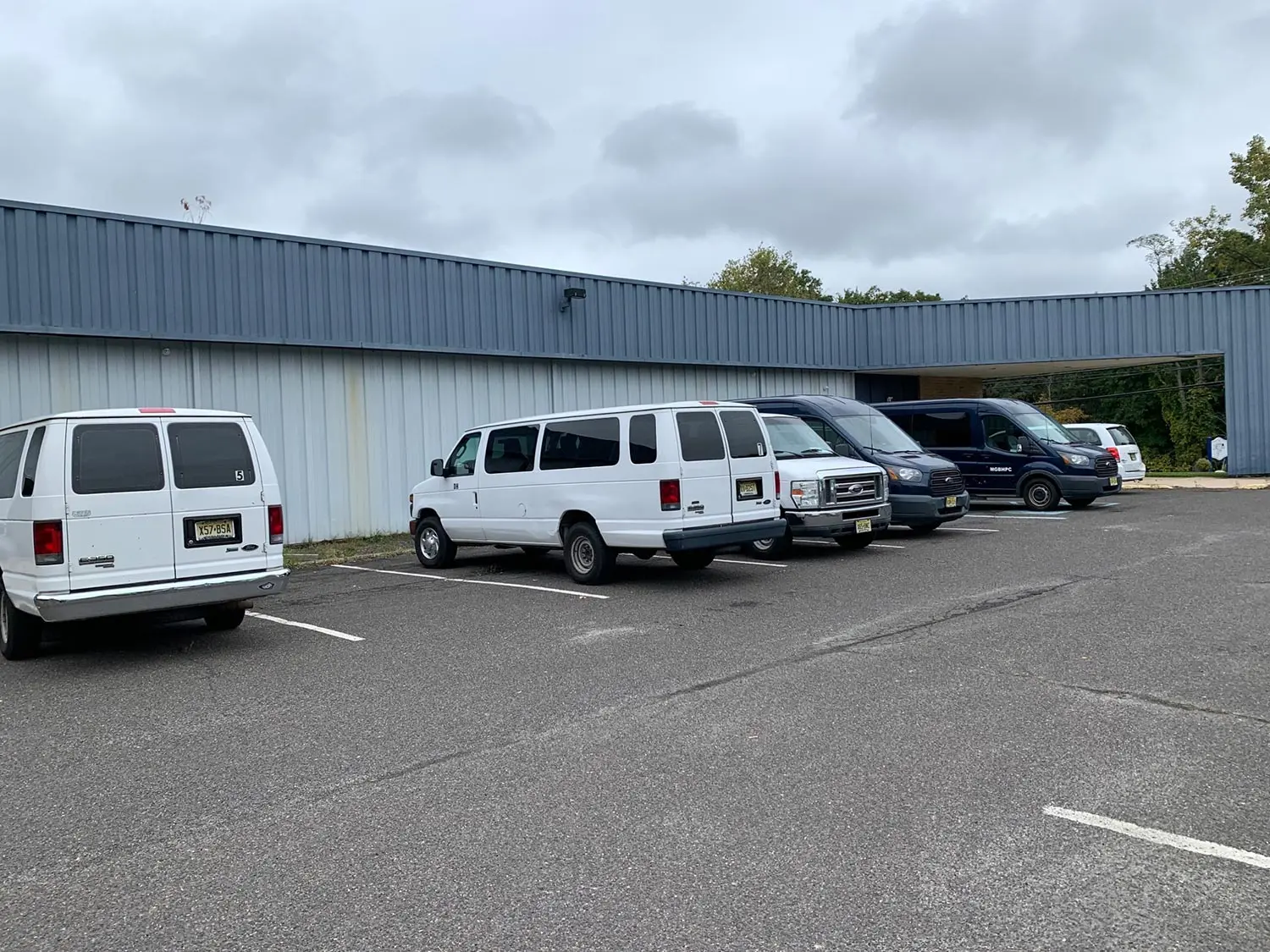 Gray metal-clad treatment center building with covered entrance and parked vans, one marked MGBHPC
