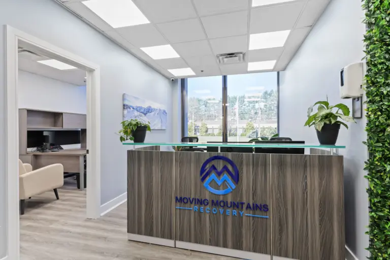 Lobby with Moving Mountains Recovery logo on a wood reception desk, plants, and a window view