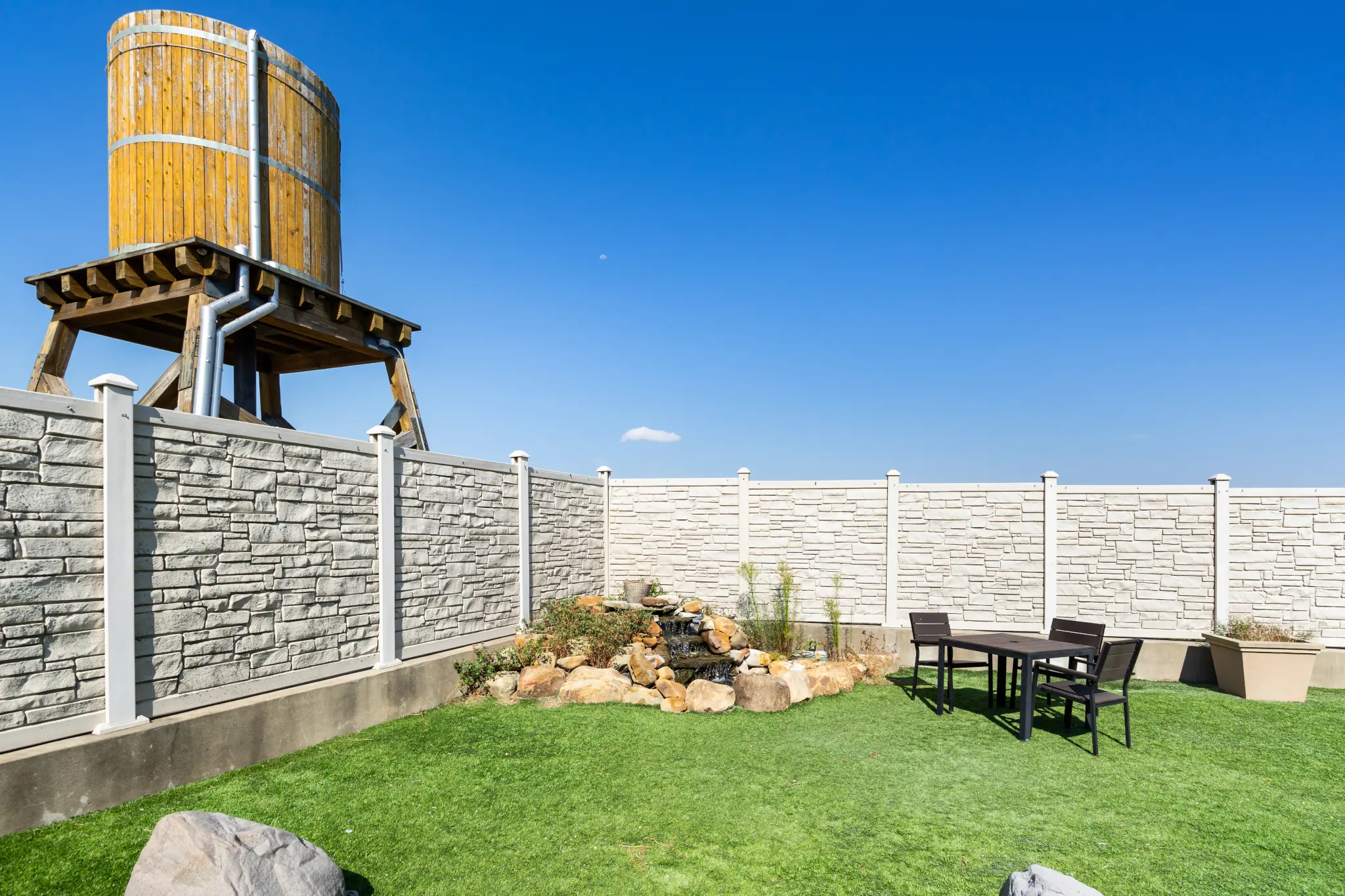 Backyard garden with a rock waterfall, artificial turf lawn, and a patio table set