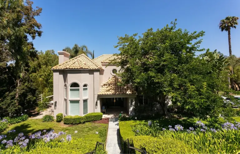 Two-story stucco building with a tile roof, a front walkway and landscaped gardens under a clear blue sky