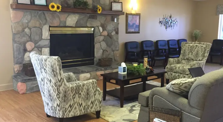 Lounge with a stone fireplace, patterned armchairs, and sunflowers on the mantel