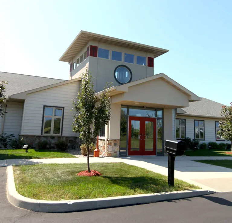 Single-story building with beige siding, a stone base, a tower, and red double entrance doors