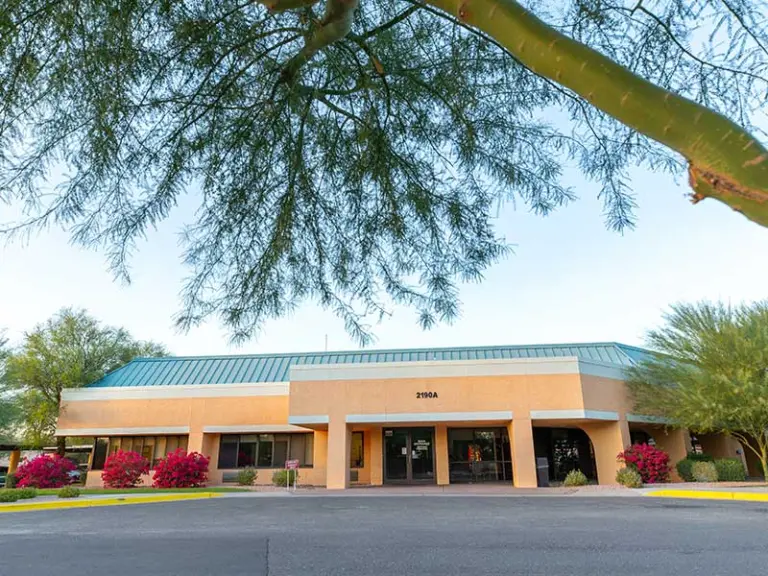 Single-story tan stucco building with teal roof and address 2190A, framed by desert trees