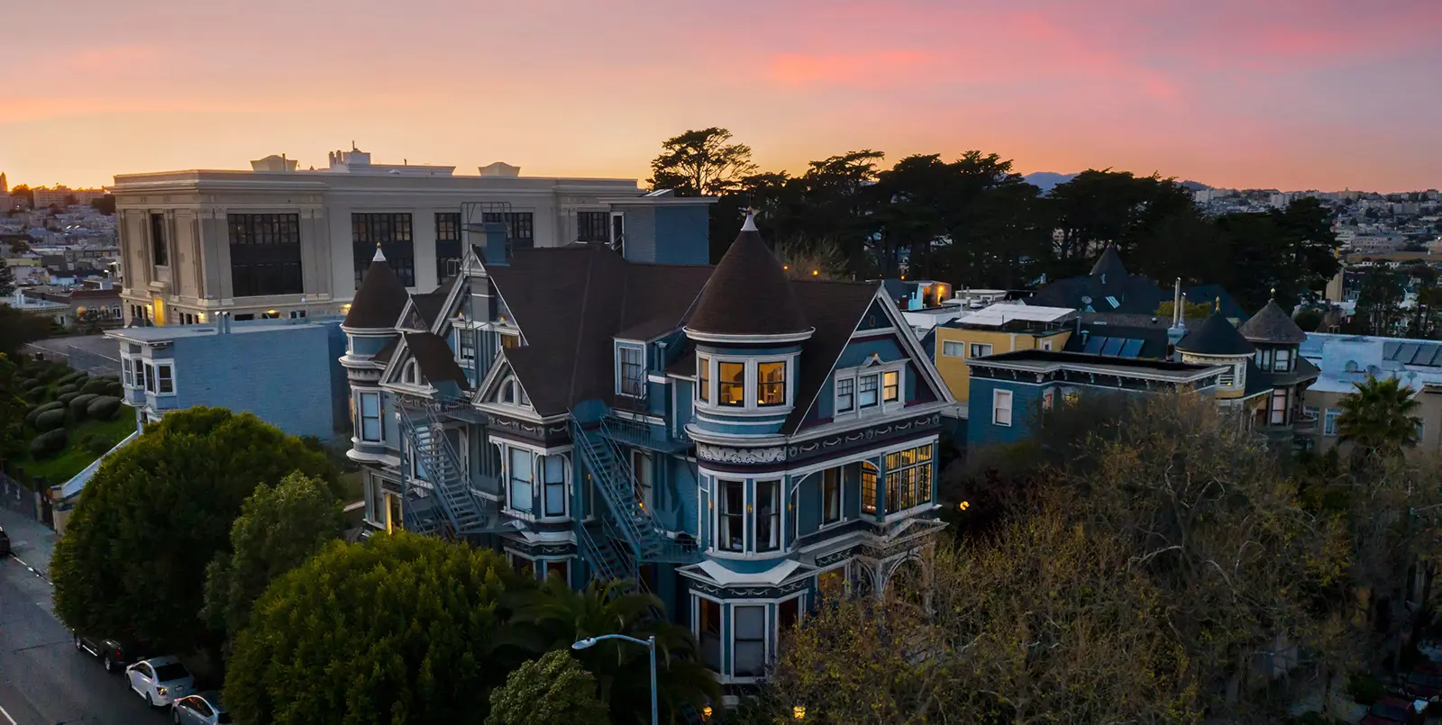 Blue Victorian mansion with a turret at sunset, viewed from above with trees in the foreground