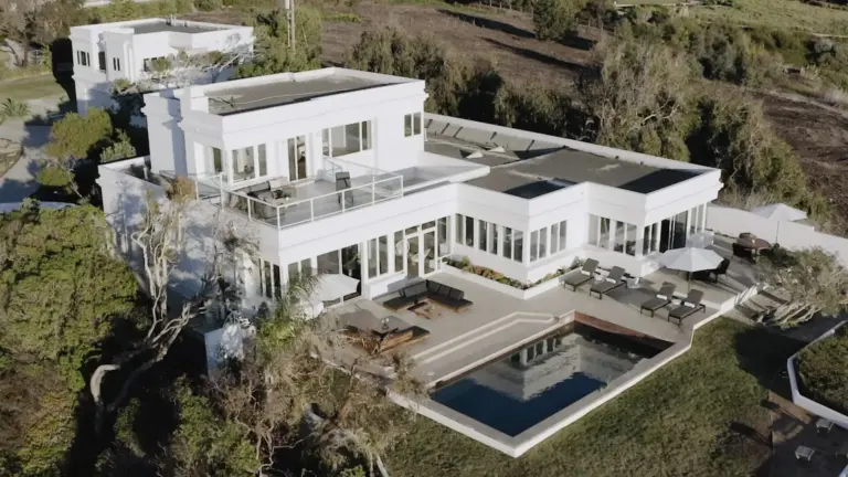 Aerial view of a white modern house with a pool and patio on a hillside property