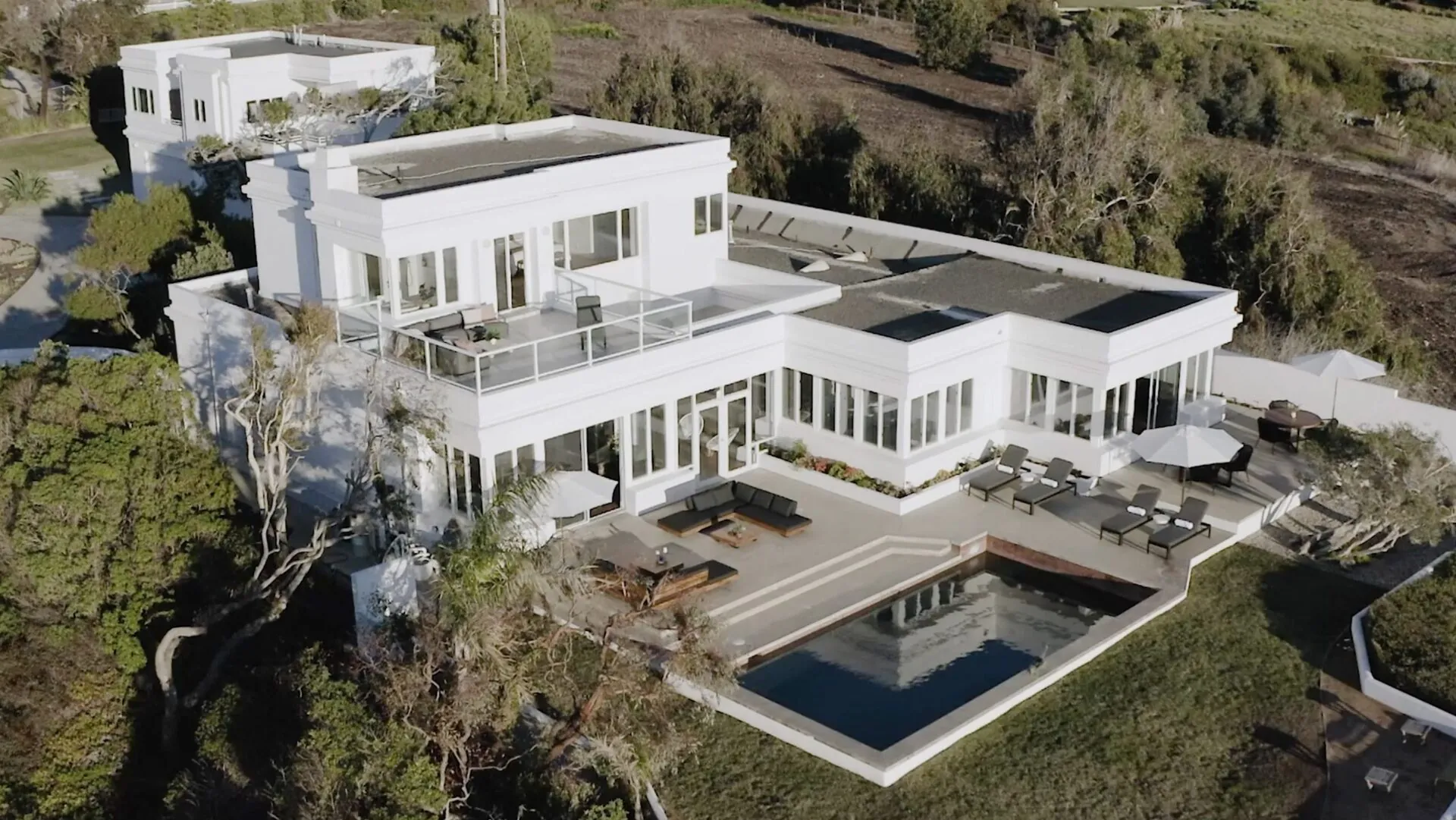 Aerial view of a white modern house with a pool and patio on a hillside property