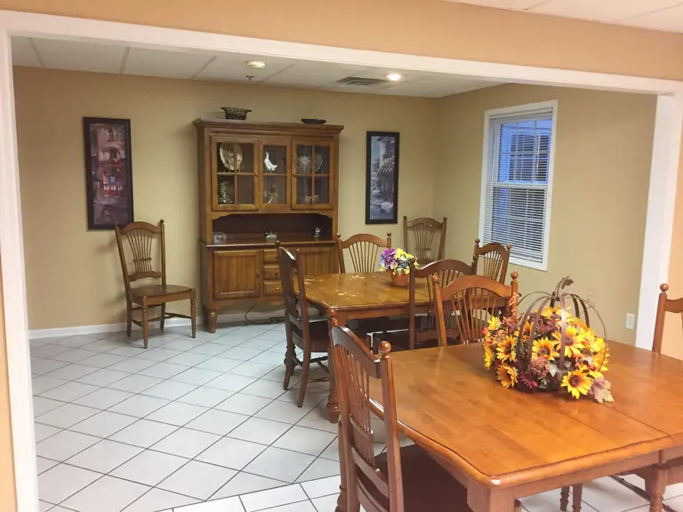 Dining room with wooden tables, chairs, a hutch, and a sunflower centerpiece
