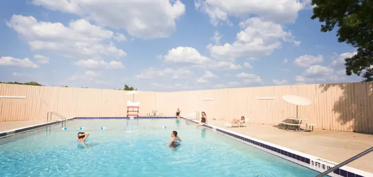 Outdoor swimming pool with blue water, tiled edge, and a tan wooden fence behind it