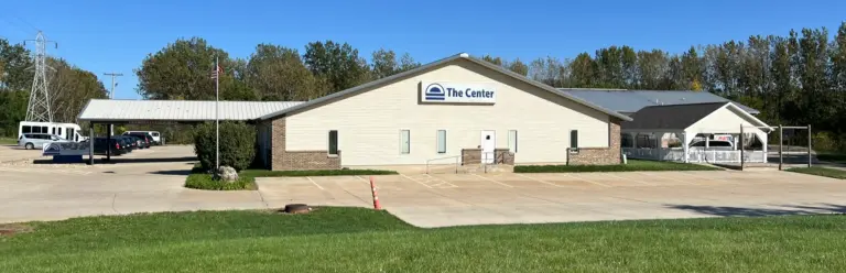 Single-story tan building with a brick base and a The Center sign, with a parking lot in front