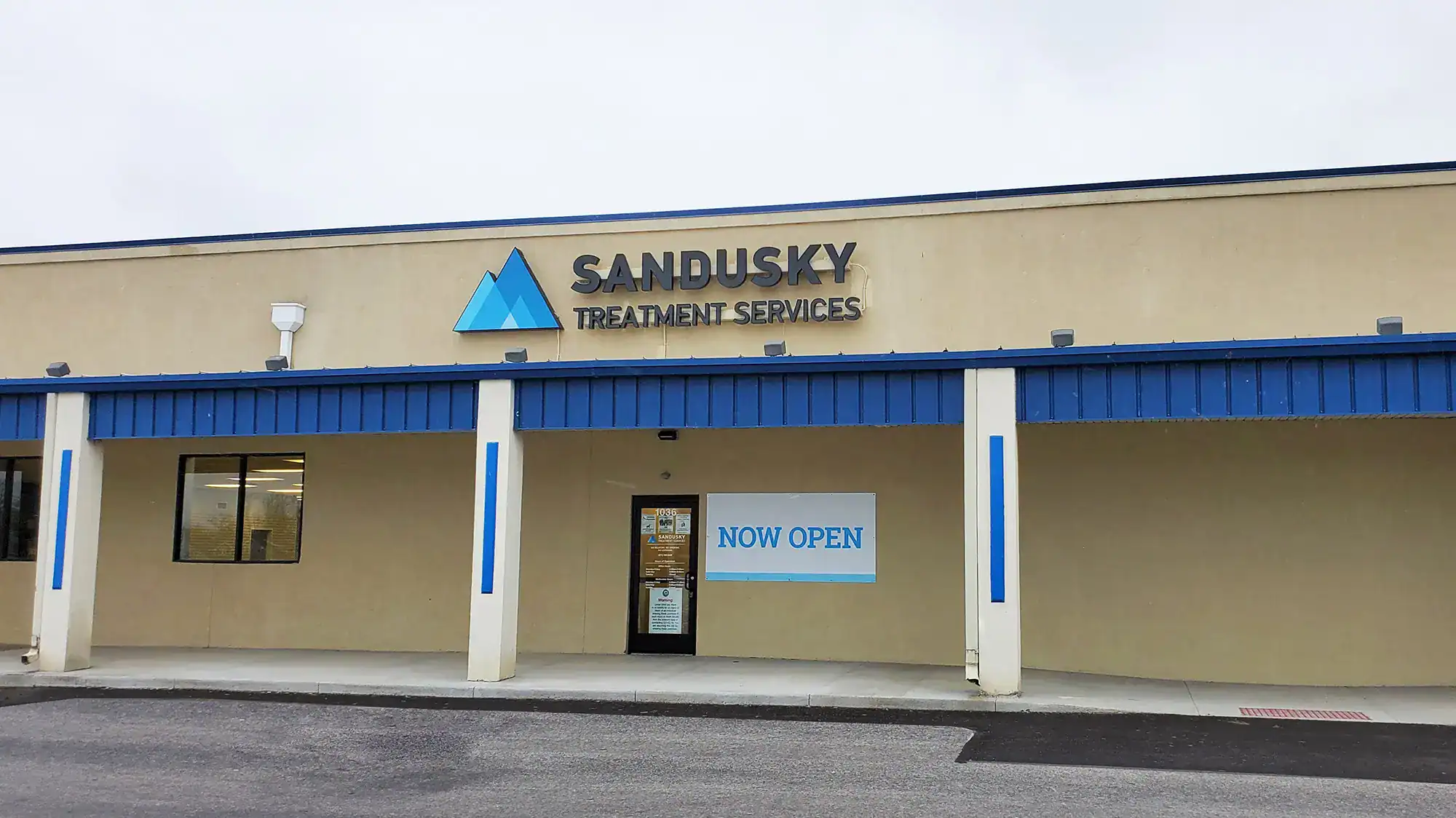 Single-story tan building with a Sandusky Treatment Services sign and a Now Open banner