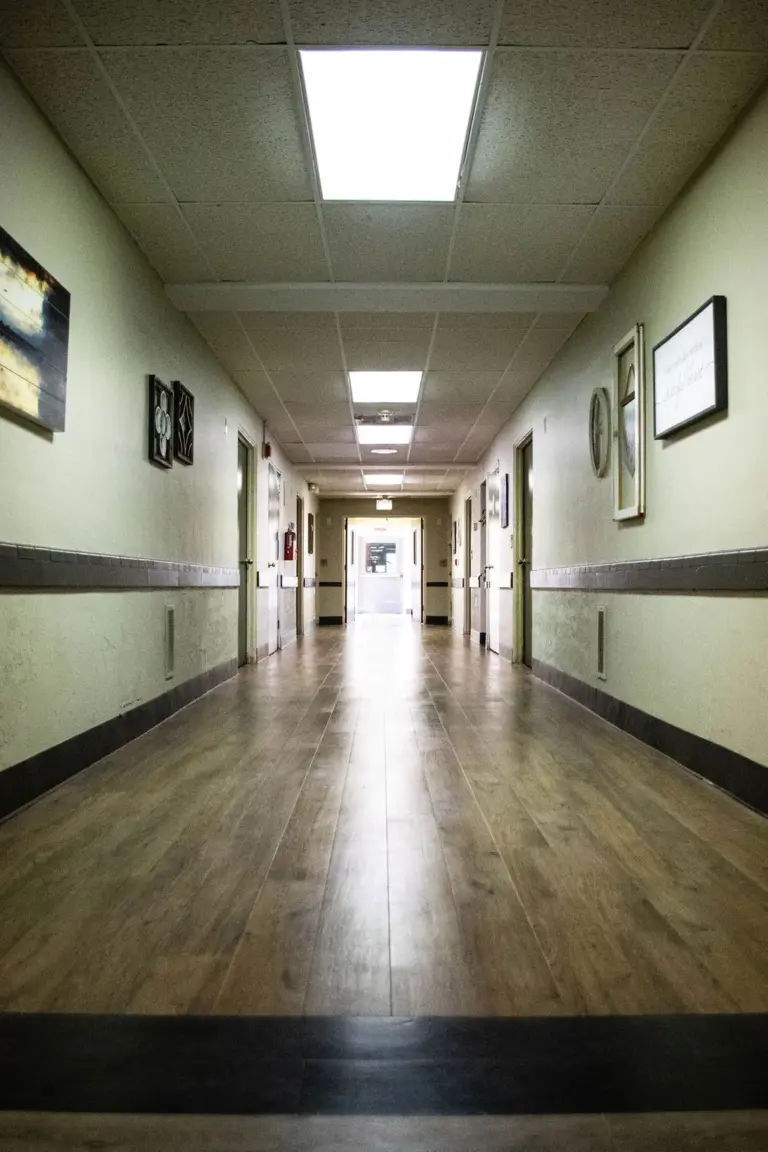 Long hallway with wood-look flooring, doors along both walls, and framed wall art
