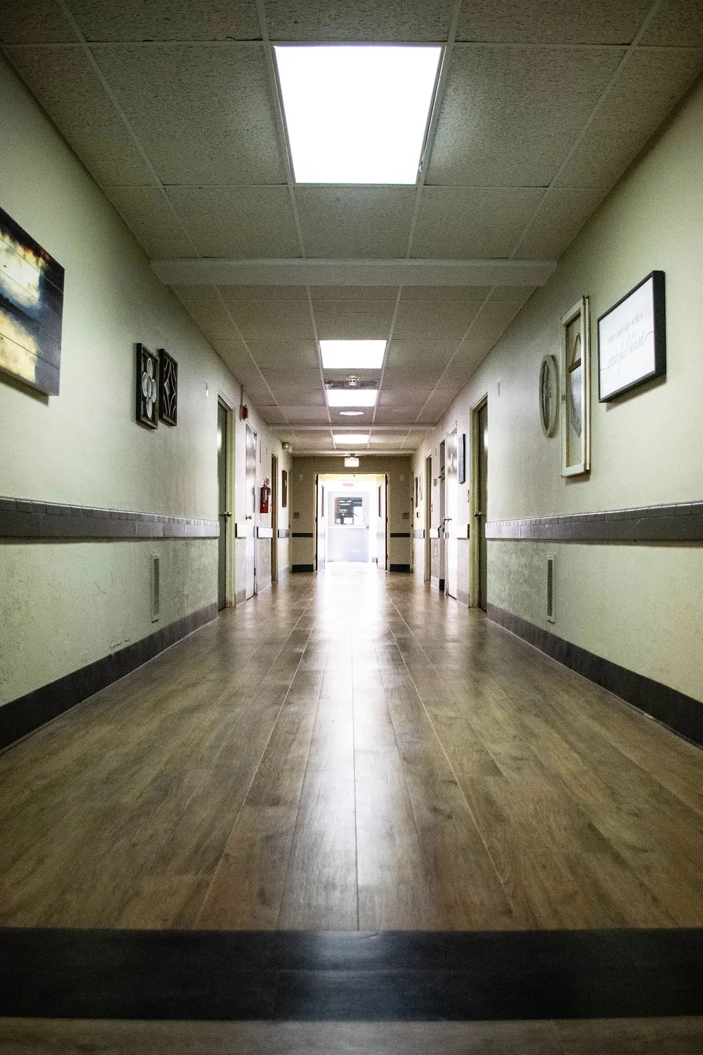 Long hallway with wood-look flooring, doors along both walls, and framed wall art
