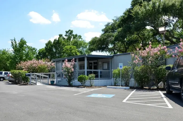 Single-story gray building with a covered porch, accessible parking, and blooming trees in front