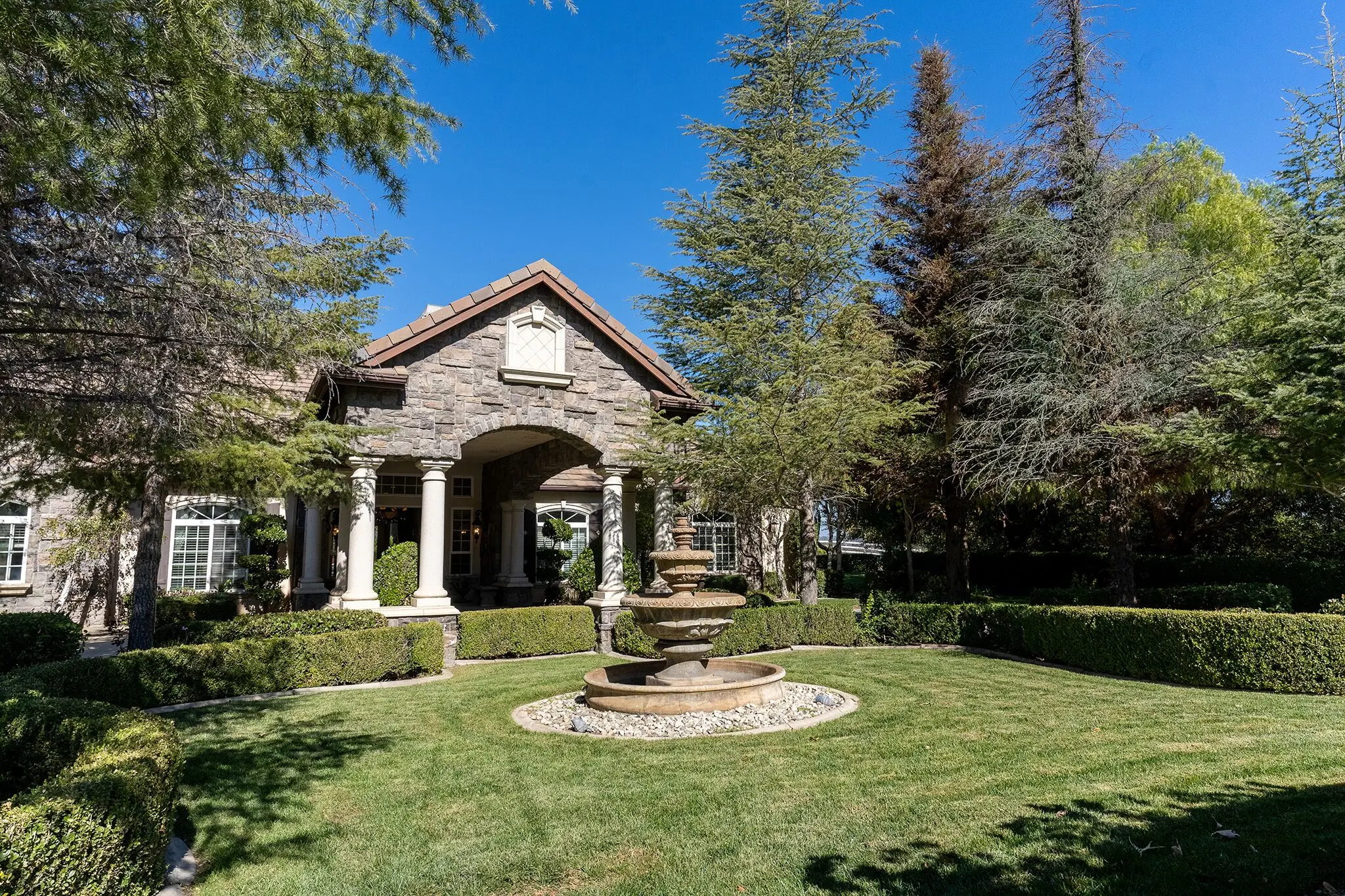 Stone and stucco residence entrance with columns, a fountain and a manicured front lawn