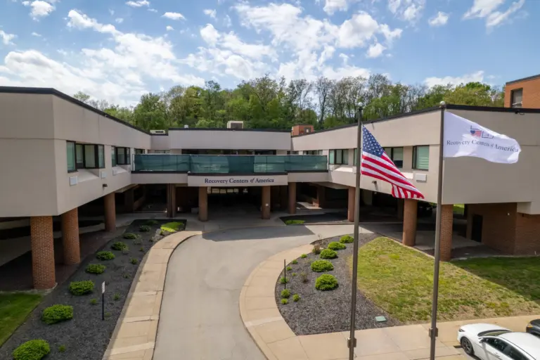 Two-story building entrance with a Recovery Centers of America sign and flags