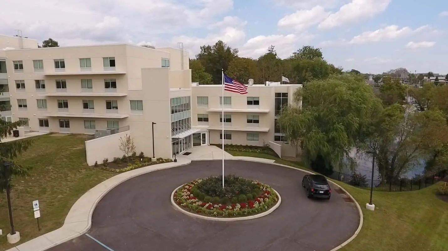 Multi-story cream building with a circular driveway, flower bed, and American flag