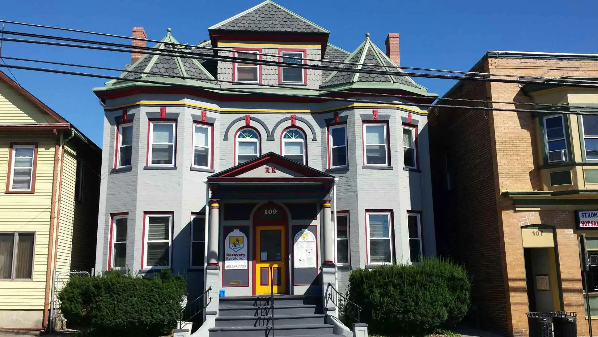 Gray Victorian-style building with red trim and a Recovery Revolution sign at the entrance