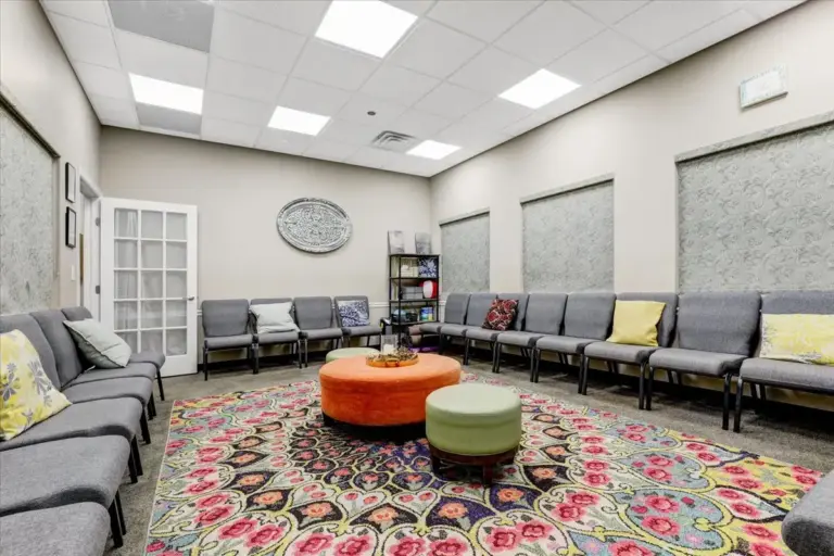 Waiting room with grey chairs, a patterned rug, and an orange ottoman at Relevance in Freehold