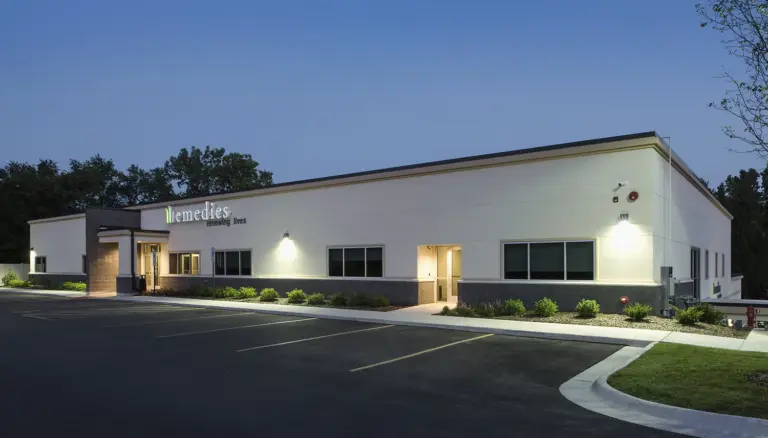 Single-story white building with a Remedies renewing lives sign and entrance lit at dusk