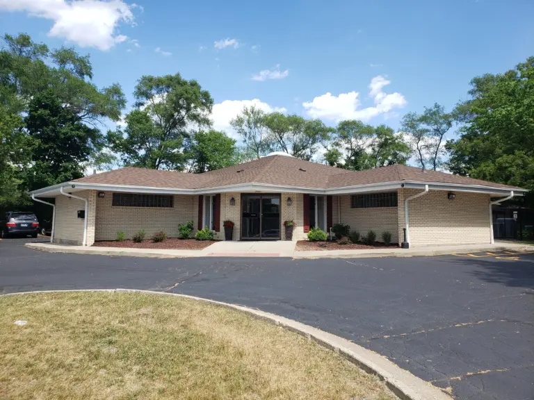 Single-story tan brick building with a central entrance and landscaped front beds under a blue sky