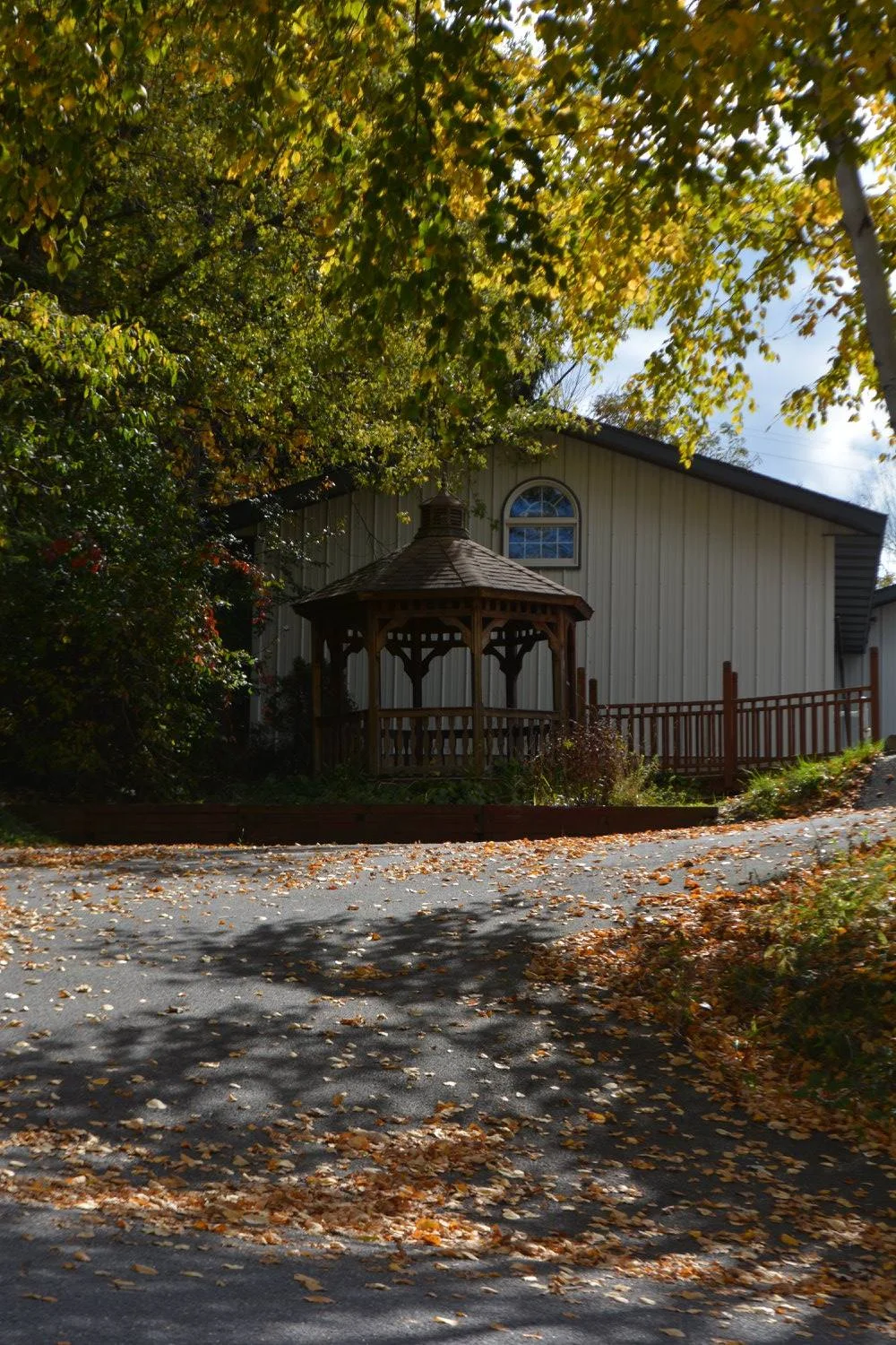 White building with a wooden gazebo and fall trees beside a driveway