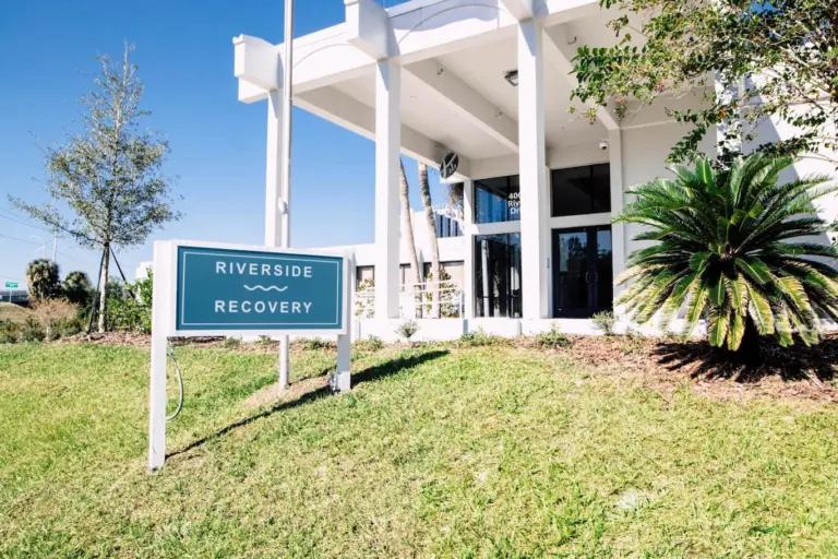 White two-story building entrance with a Riverside Recovery sign on the lawn