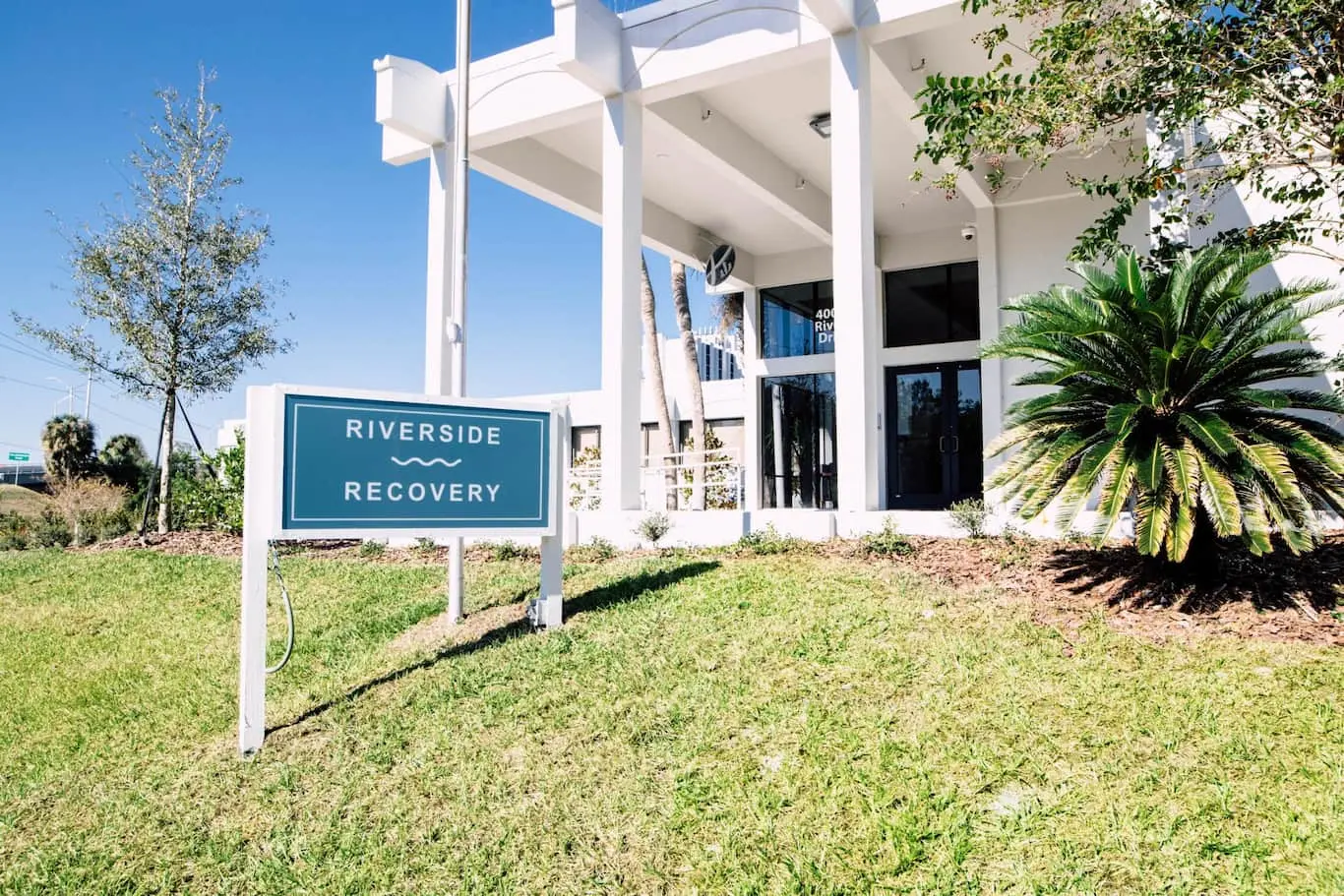 White two-story building entrance with a Riverside Recovery sign on the lawn