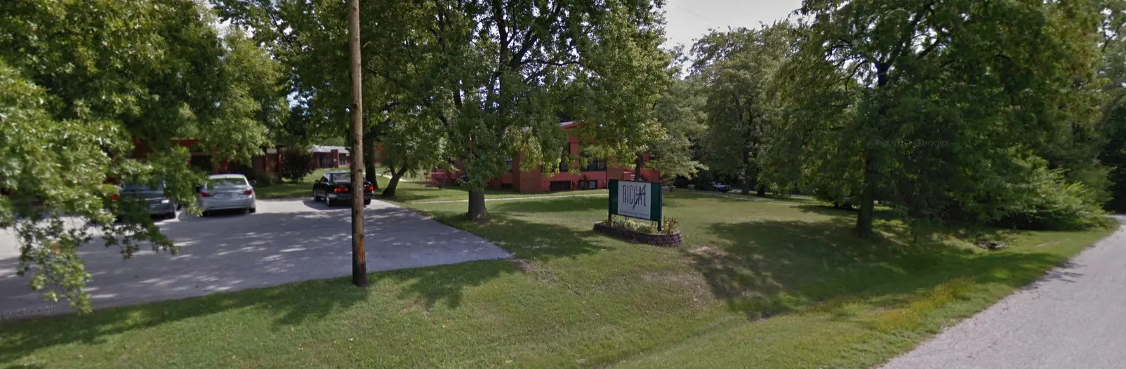 Brick building behind a lawn with a green Ricca sign at the street