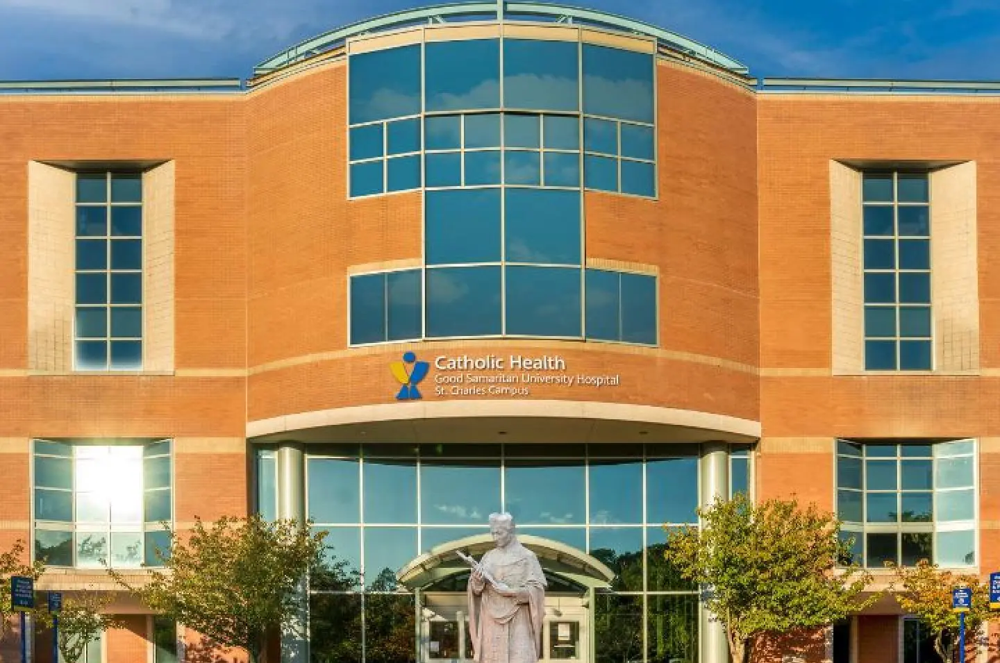Brick hospital facade with Catholic Health Good Samaritan University Hospital St. Charles Campus signage over the entrance