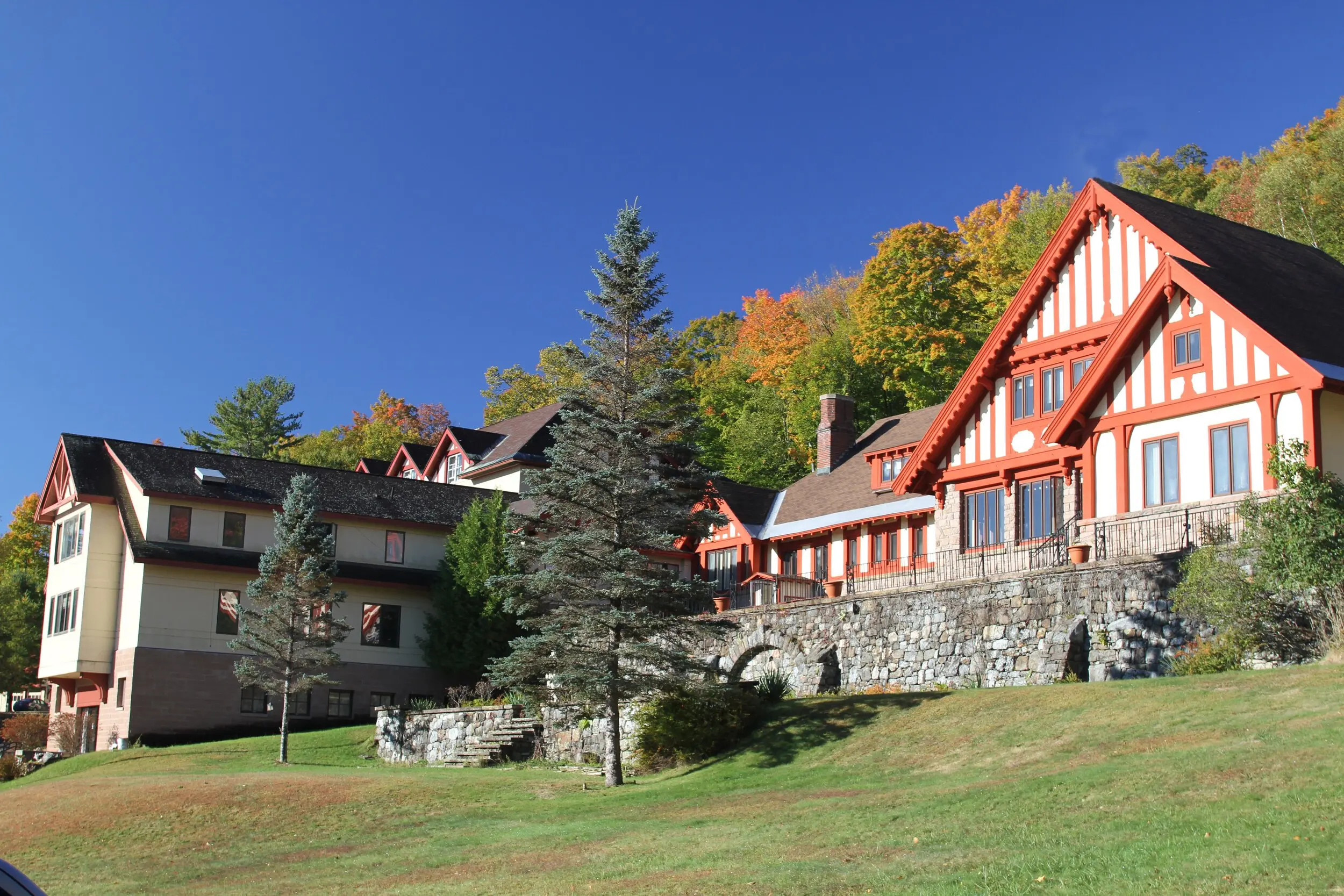 Multi-building campus with a red and white half-timbered main building, stone wall, and autumn trees