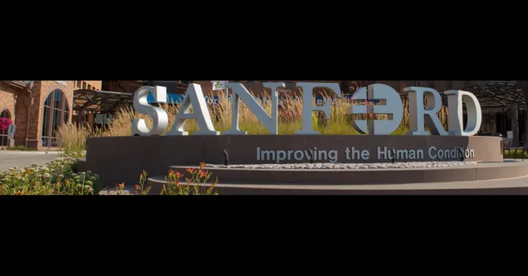 Large Sanford Health monument sign reading Improving the Human Condition in front of a brick building