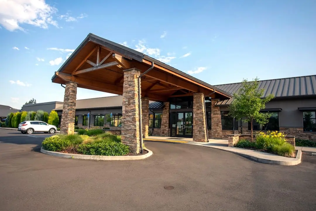 Stone-columned entrance canopy of a one-story treatment center building with landscaped drive and parked car