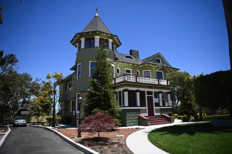 Green Victorian house with a turret, red front door and white porch railings under a blue sky