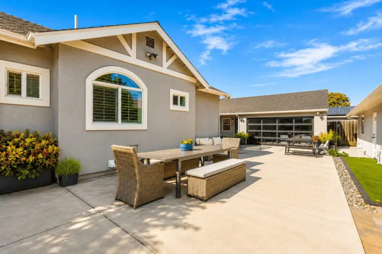 Patio with wicker dining set and sofa beside a gray stucco building with arched window
