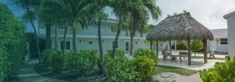 Palm-lined two-story white building and thatched palapa on the Singer Island Health campus grounds