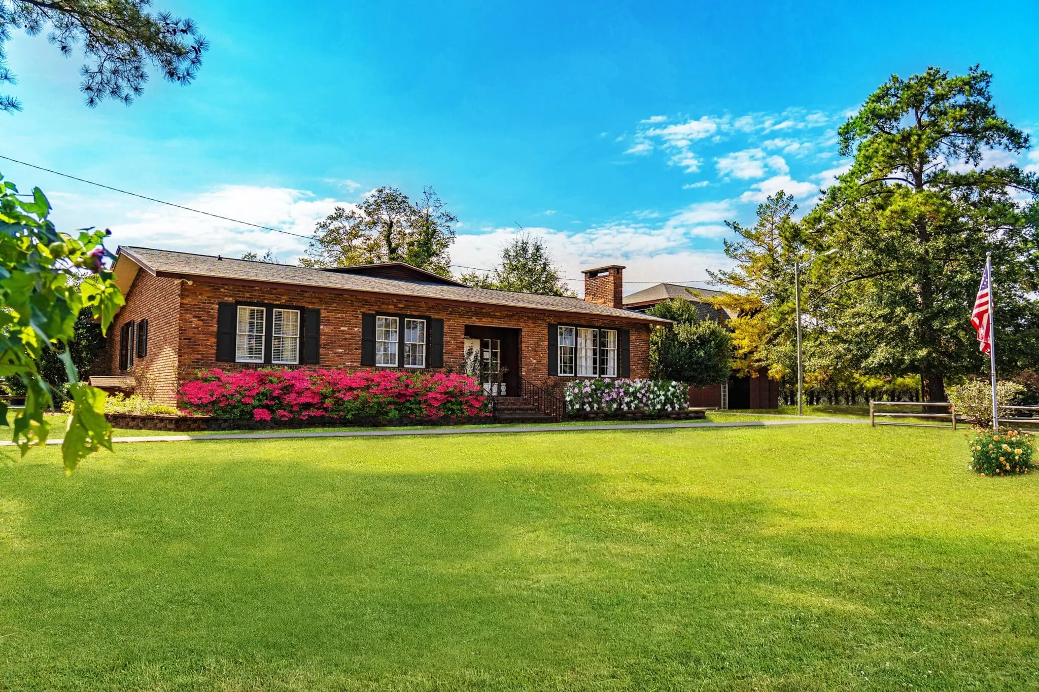 Single-story brick building with red azalea bushes, green lawn, and an American flag