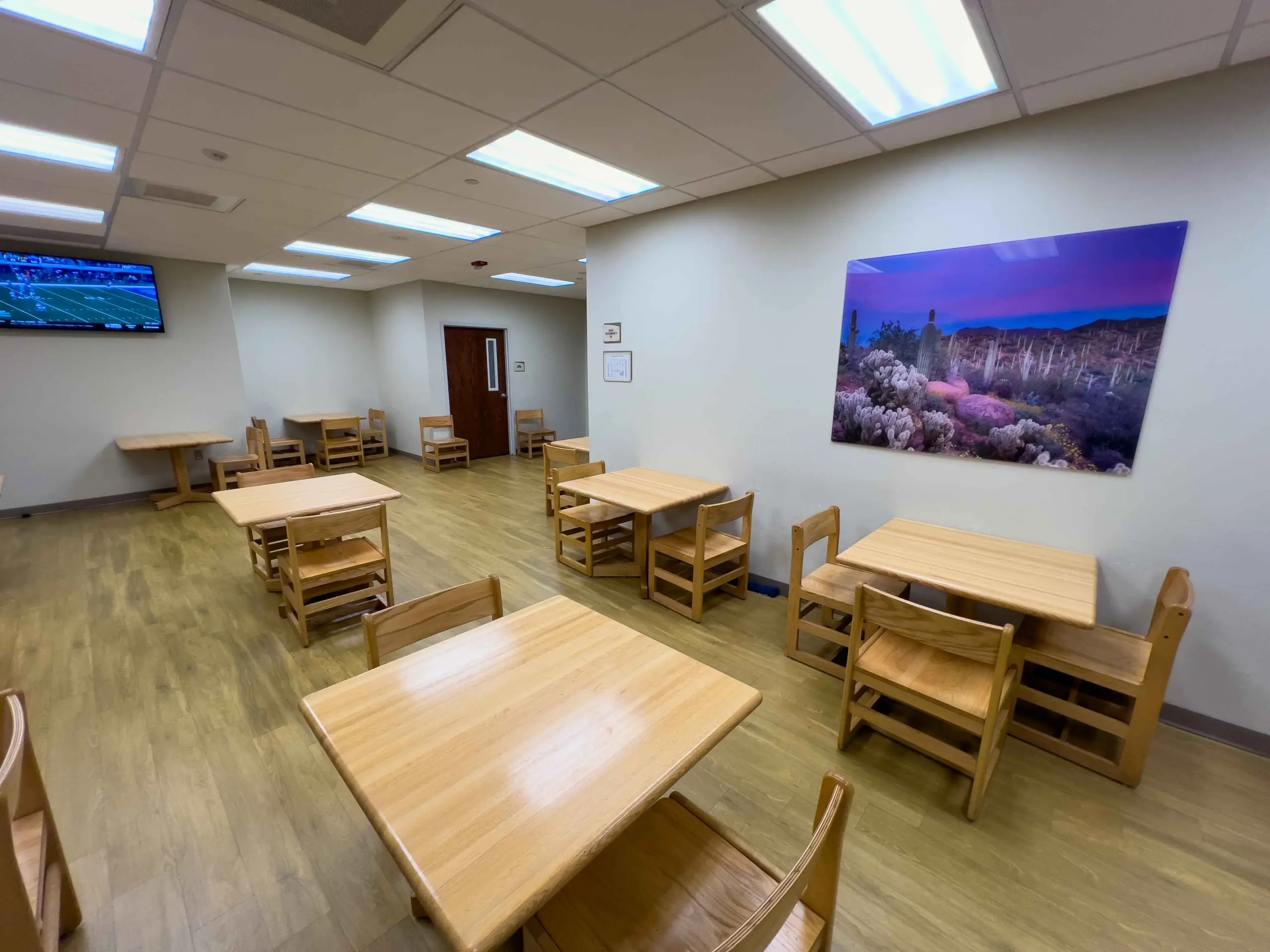 Dining room with wooden tables and chairs and a framed desert landscape on the wall