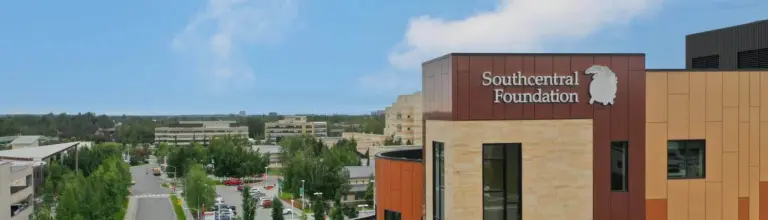 Southcentral Foundation sign on a tan and brown campus building with a city street view