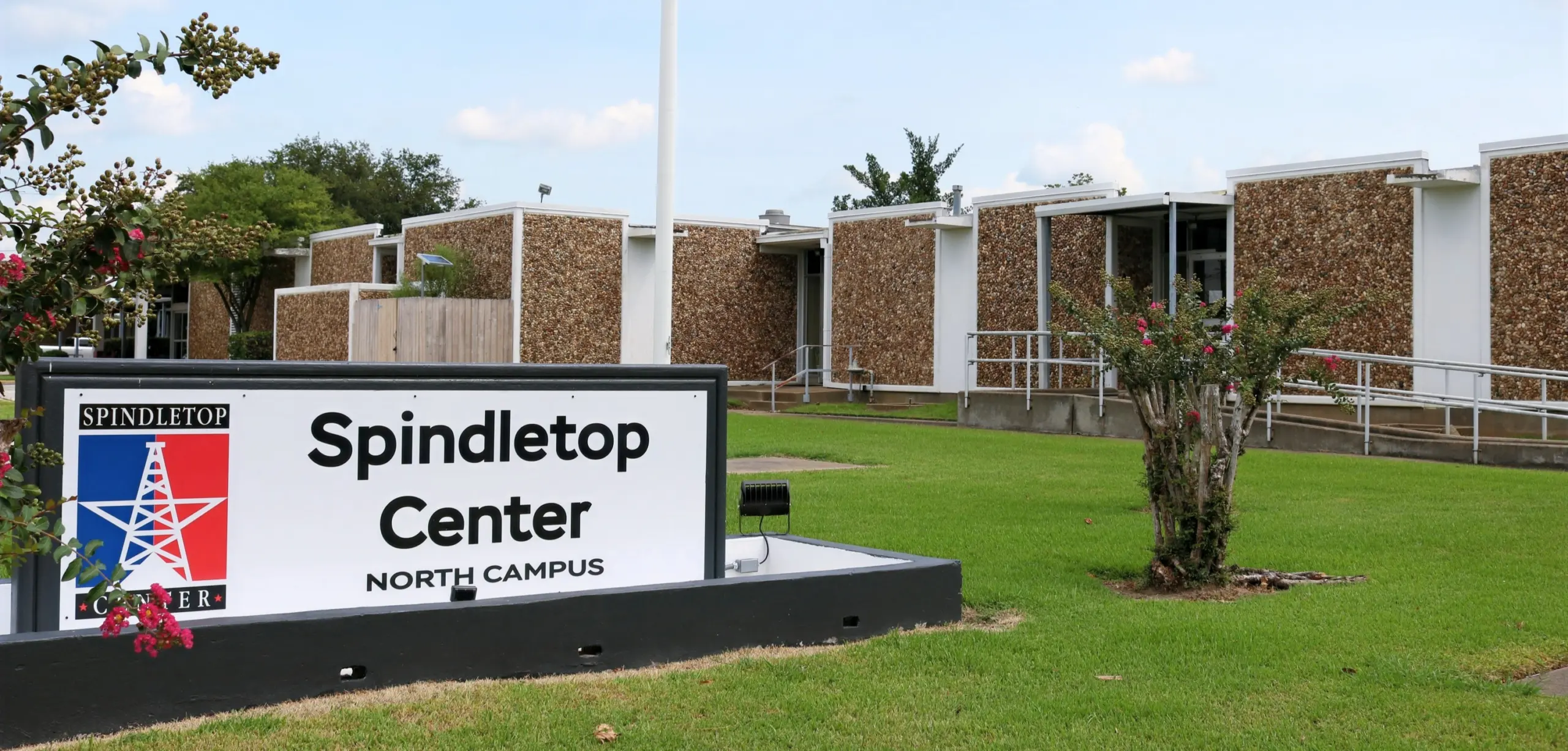 Spindletop Center North Campus sign in front of a one-story building with brick-patterned walls and a lawn