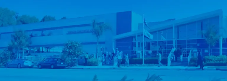 Blue-tinted two-story building with entrance steps, a flagpole, and people walking outside