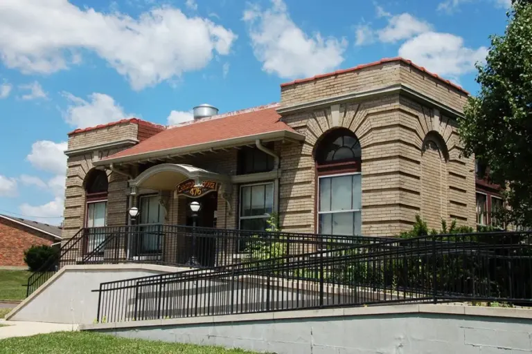 Tan brick building with red roof, entrance sign reading 476, and black metal railing and ramp