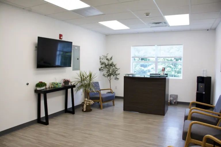Bright reception waiting room with armchairs, a wall-mounted TV, and a front desk