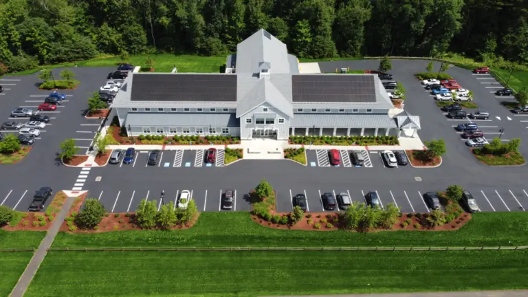 Aerial view of a two-story building with solar panels, surrounded by parking and lawns