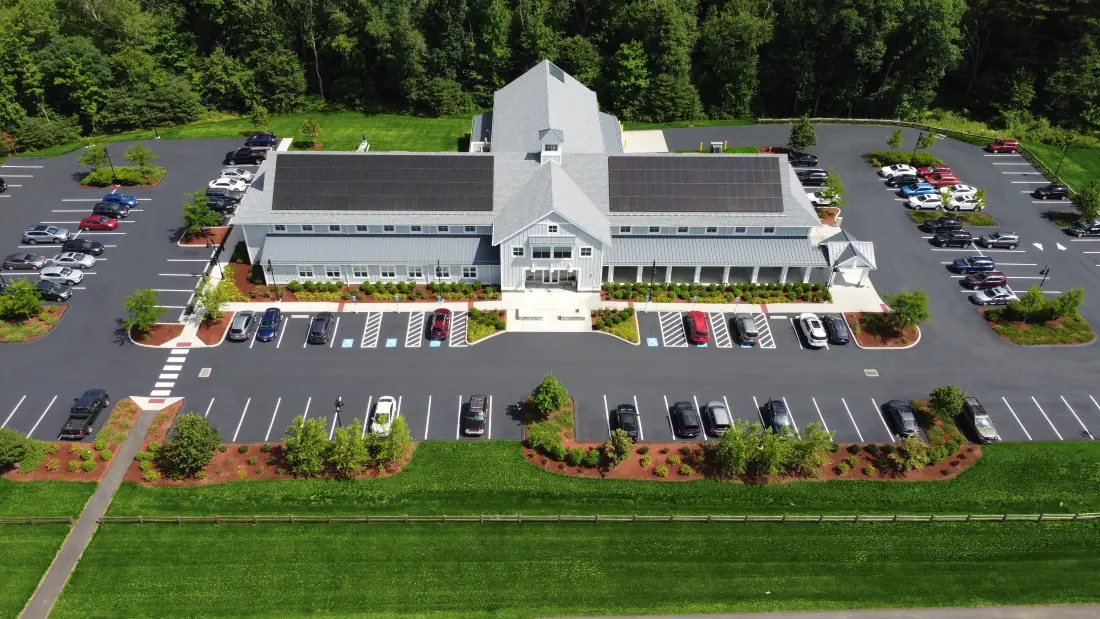 Aerial view of a two-story building with solar panels, surrounded by parking and lawns
