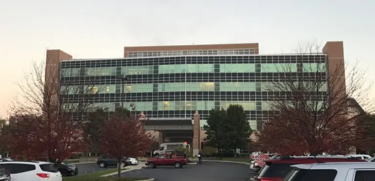 Multi-story glass-front medical building with a covered entrance and parking lot at dusk