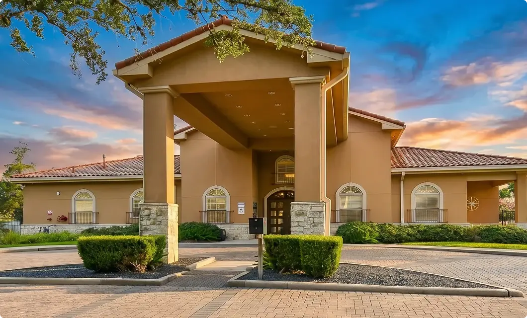 Tan stucco building entrance with a covered portico, arched windows, and a brick driveway